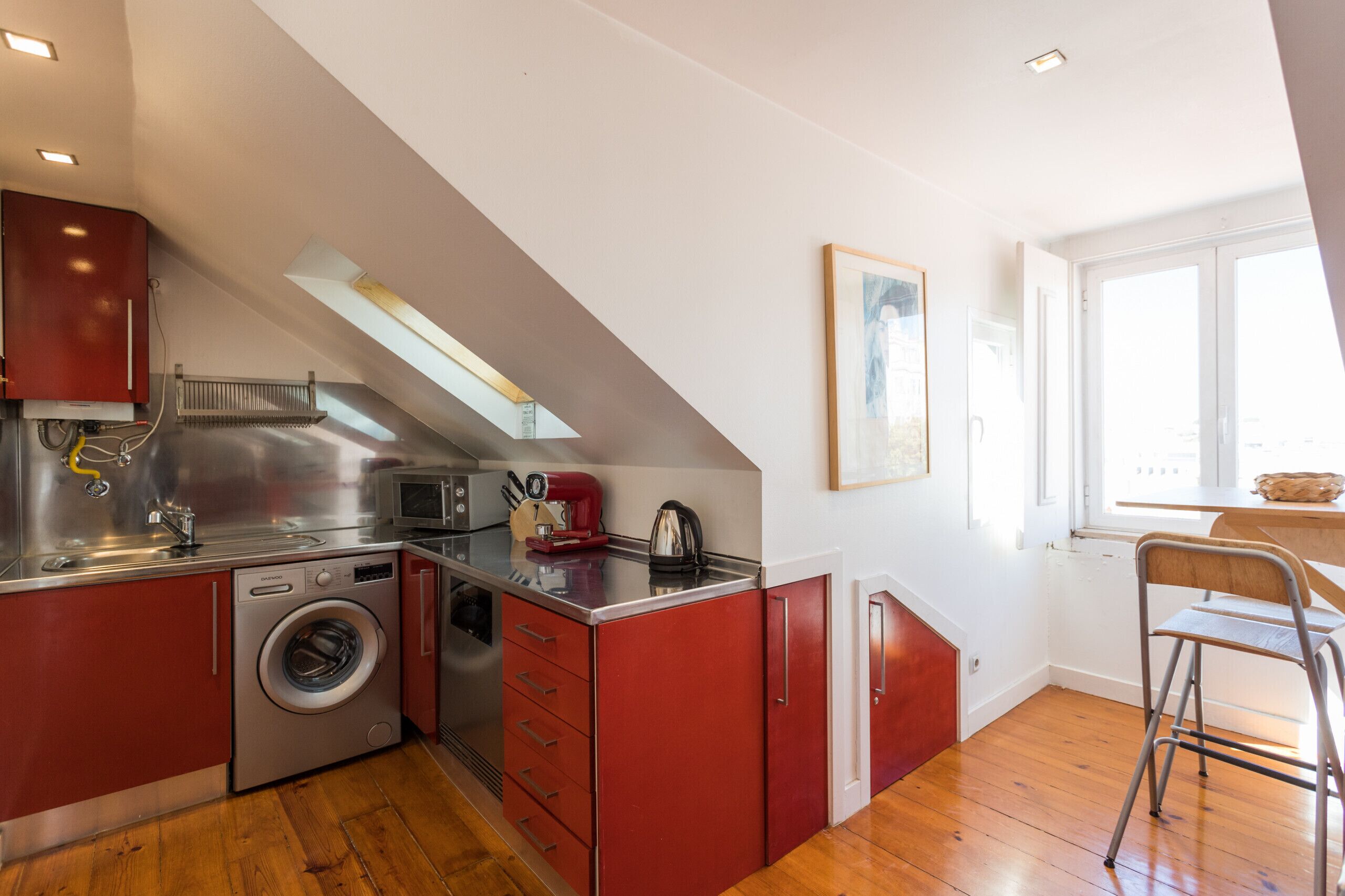 Een kleine keuken met een wasmachine, een magnetron en een rode kast.
