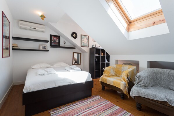A bedroom with a bed, a chair, a sofa, a fireplace, and a skylight.