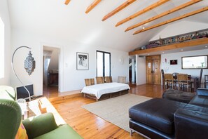 A spacious room with a bed, a green armchair, a black leather sofa, wooden beams on the ceiling, and a dining area with chairs and a table. - FLH Chiado Skyline (Lisbon)