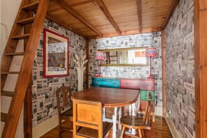 Cozy retreat with a wooden dining table, bench, and ladder, surrounded by personal touches and a unique newspaper-clipping wall.