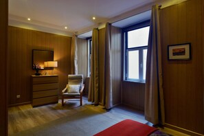 Une chambre d’hôtel avec des lambris en bois, un lit, une chaise, une commode, une fenêtre avec des rideaux et un tableau encadré au mur.