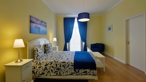 Ein Schlafzimmer mit Bett, Nachttischen, Schreibtisch, Sessel, Pendelleuchte und einem Bild an der Wand.