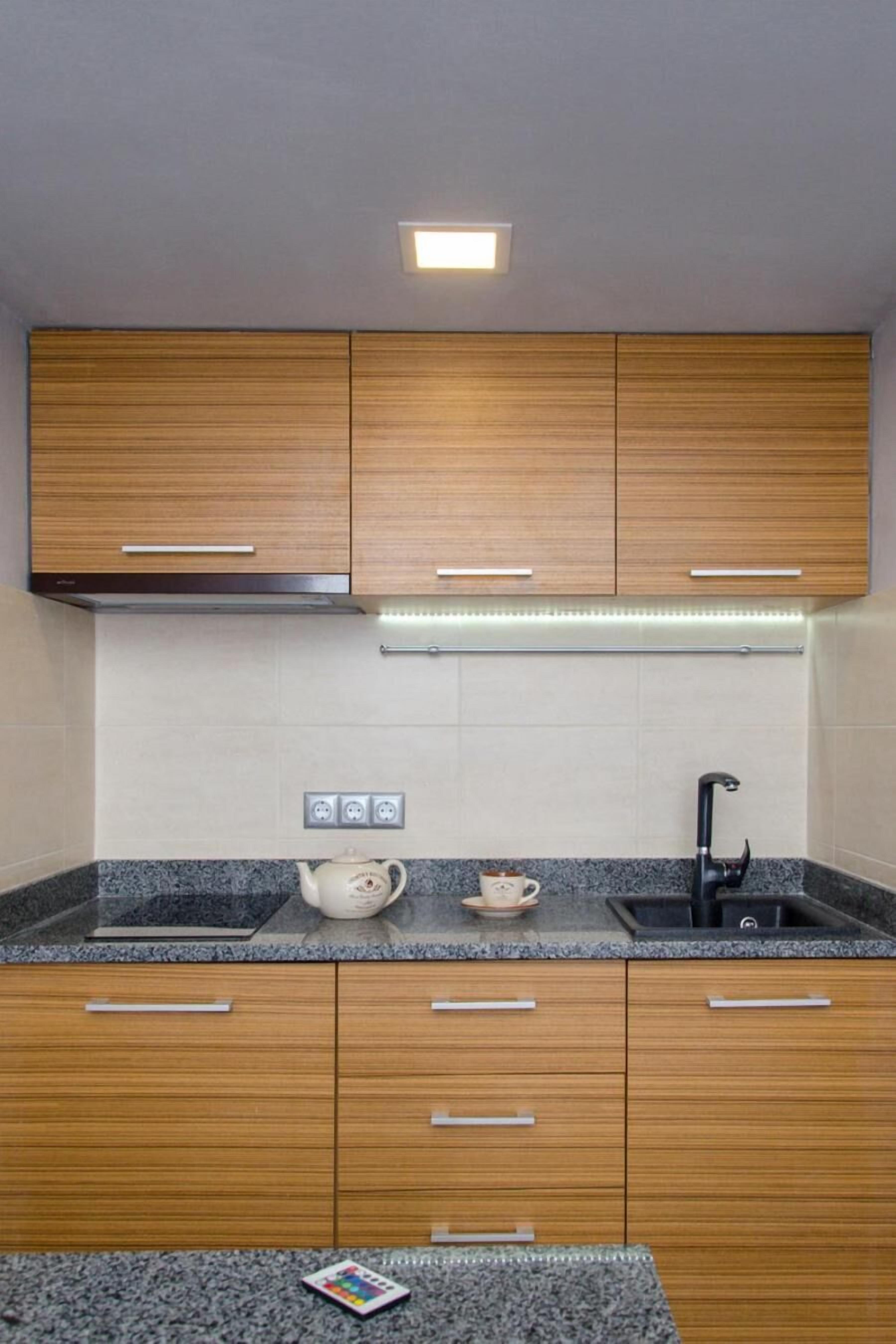 A modern kitchen with wooden cabinets, a granite countertop, a kettle, a cup, and a black faucet.