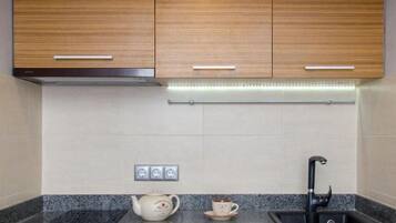 A modern kitchen with wooden cabinets, a granite countertop, a kettle, a cup, and a black faucet.