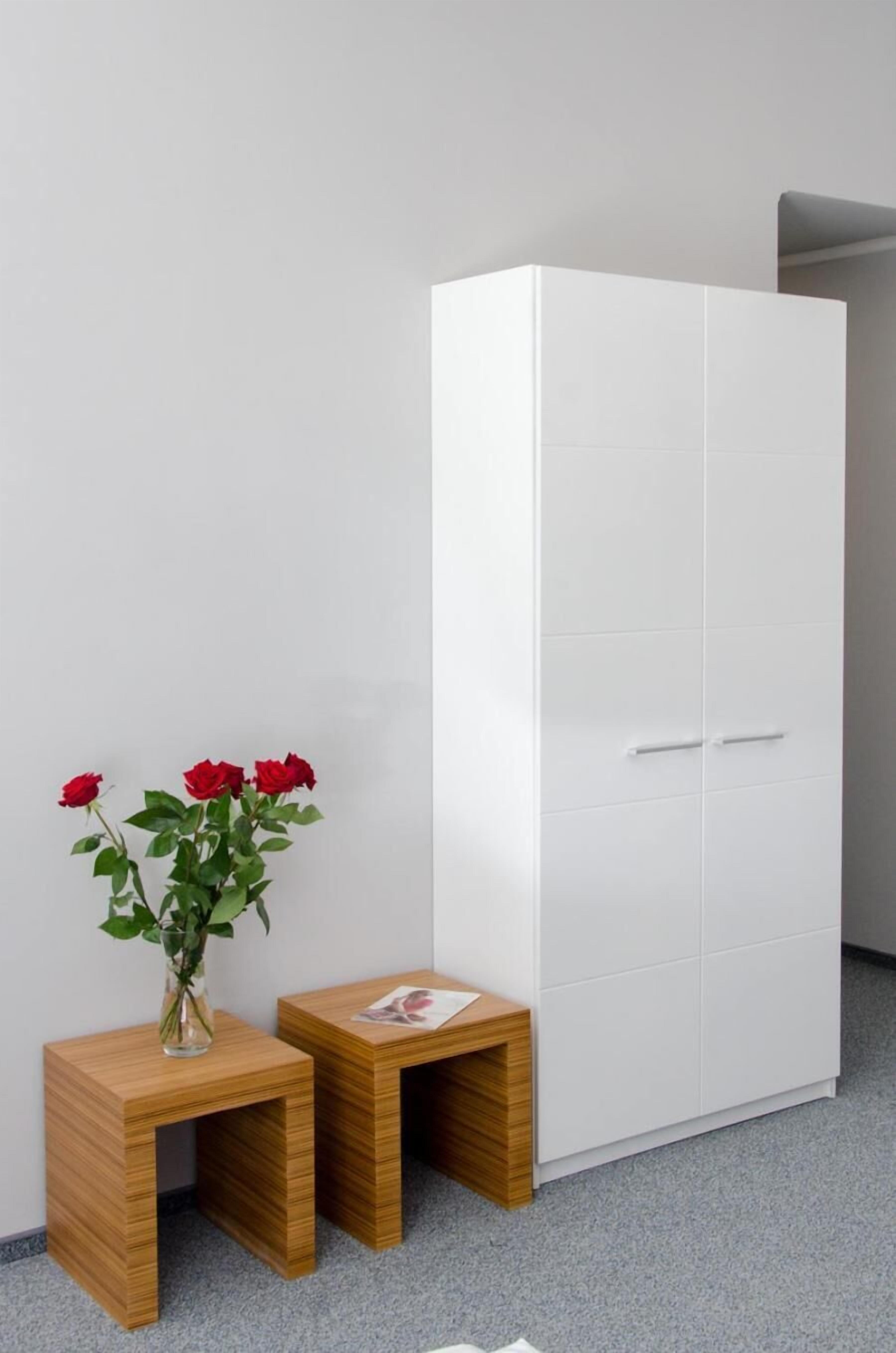 Une armoire blanche à deux portes et une petite table en bois sur laquelle est posé un vase de roses rouges.