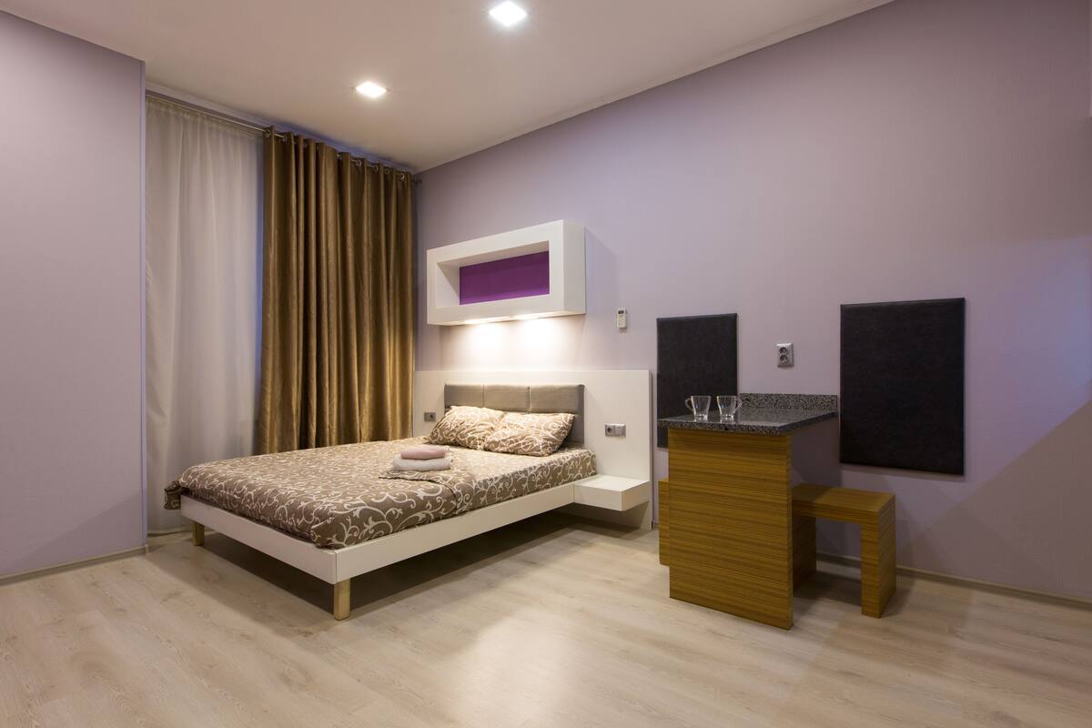 A modern bedroom with a bed, bedside table, and a small wooden stool.