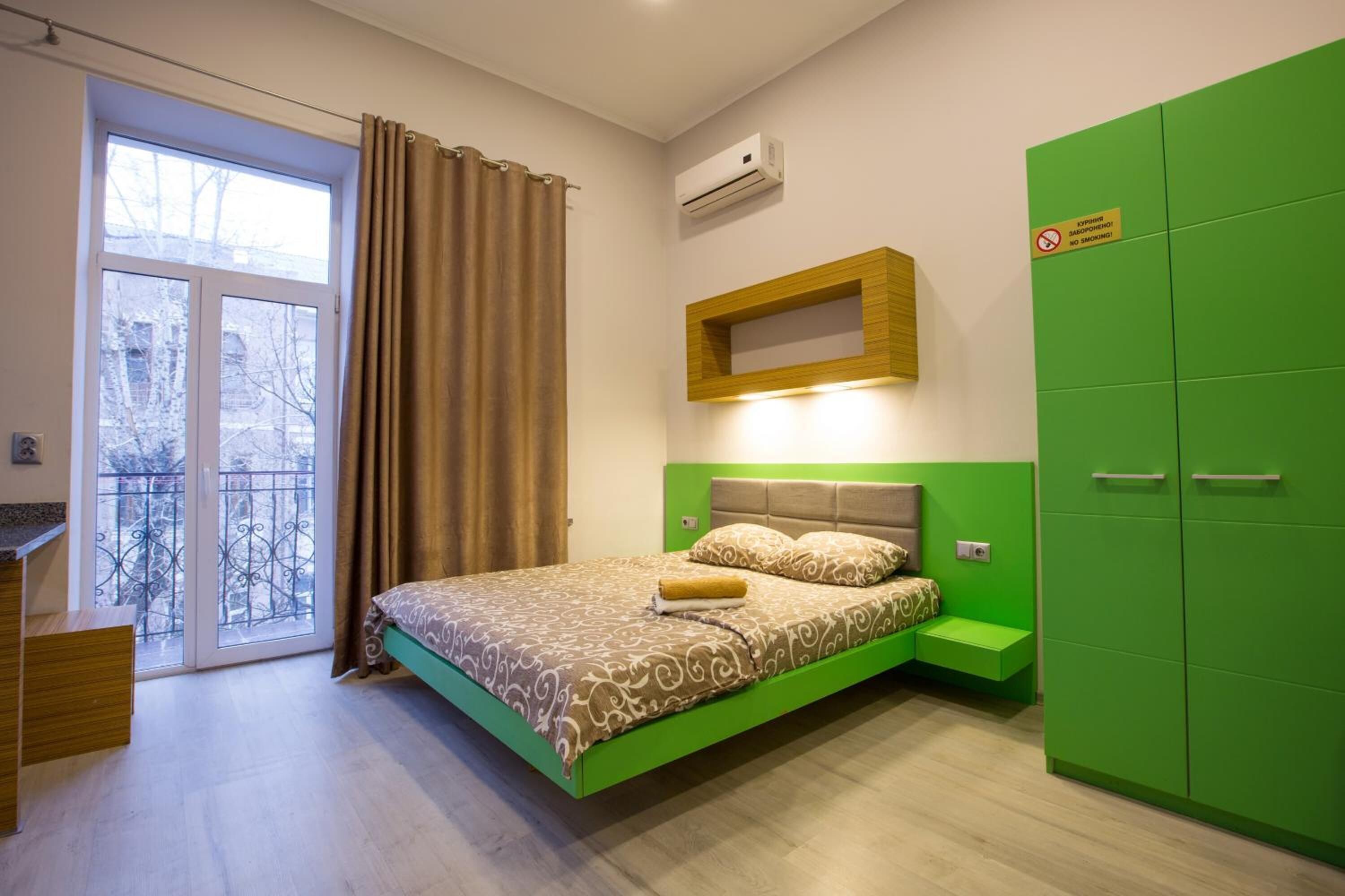 A bedroom with a bed, a green wardrobe, a small bedside table, and a window with curtains.