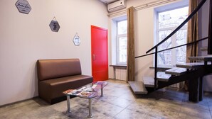 Una zona de recepción con un sofá marrón, una puerta roja y una escalera.