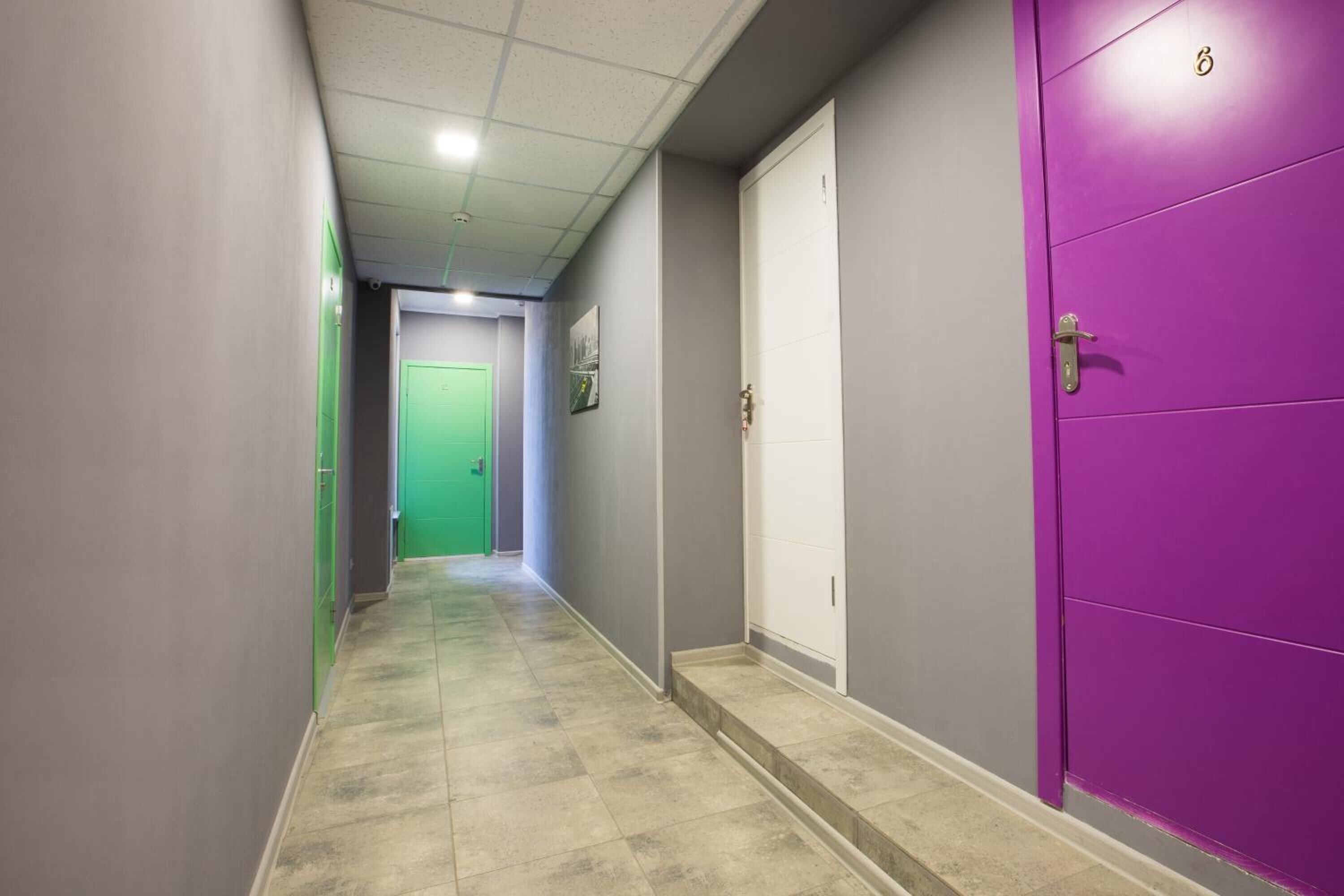 A hallway with a green door at the end, a purple door to the right, and a white door further down.