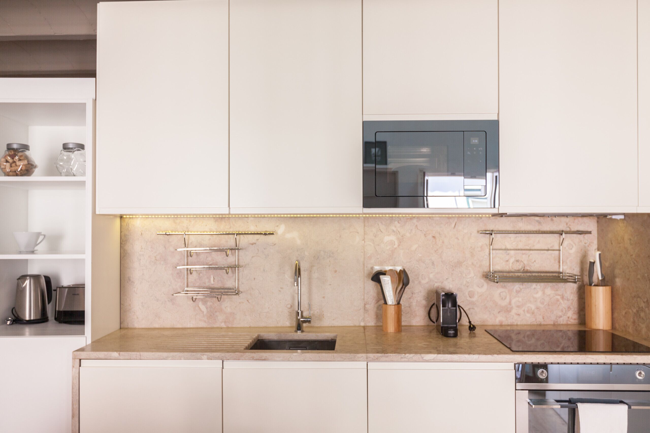 Una cucina moderna con mobili bianchi, un lavello in acciaio inossidabile, un forno a microonde e una macchina da caffè.