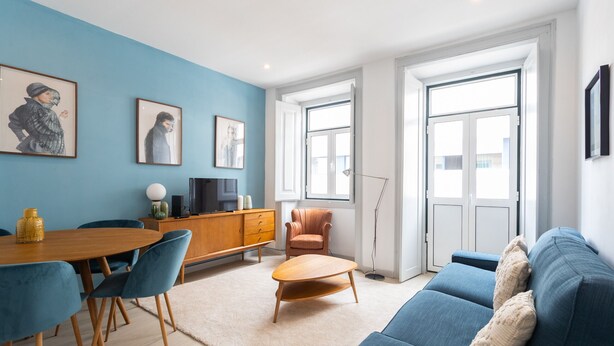 A modern living room with a blue sofa, a wooden coffee table, and a dining area with a wooden table and chairs. - FLH Lx Factory Charming Place (Lisbon)