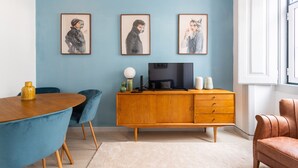 A modern living room with a blue wall, a wooden TV stand, a round dining table, and blue chairs. - FLH Lx Factory Charming Place (Lisbon)