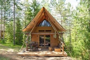 Een houten chalet met een puntig dak, een terras met zitplaatsen en een groot raam.