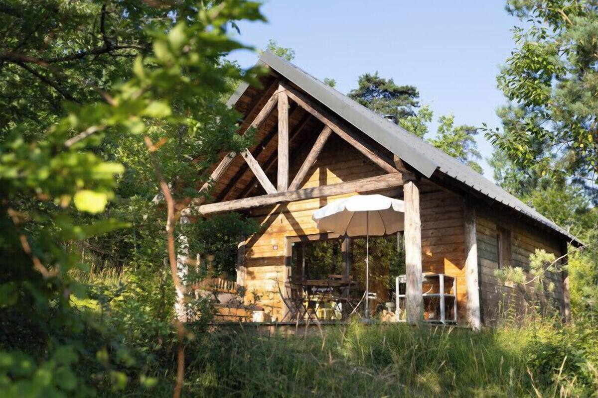 A rustic wooden cabin with a pitched roof, a porch with a table and chairs, and a small window.