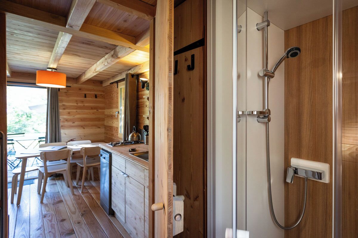 A wooden cabin interior with a kitchen area, dining table, and a shower.