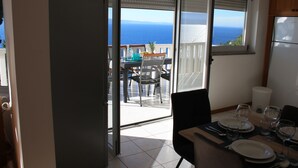 A dining area with a table set for four, a view of the sea through a sliding glass door, and a refrigerator in the corner. - Villa Blue Adriatic (Omis)