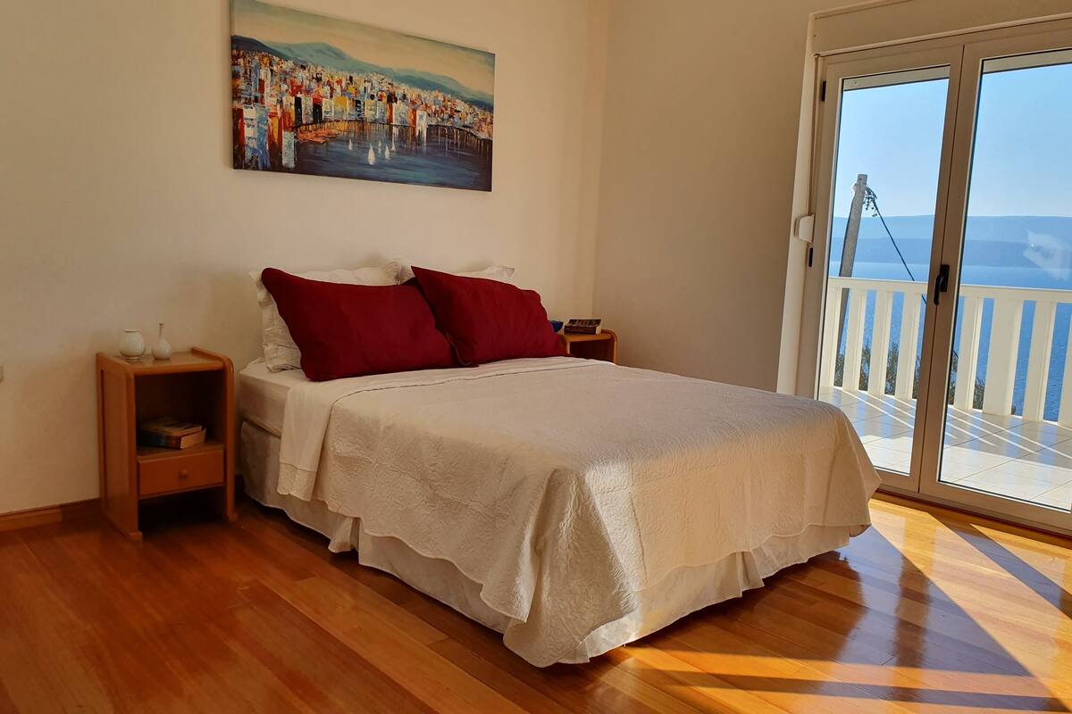 Un dormitorio con cama, mesita de noche, un cuadro y un balcón con vistas.