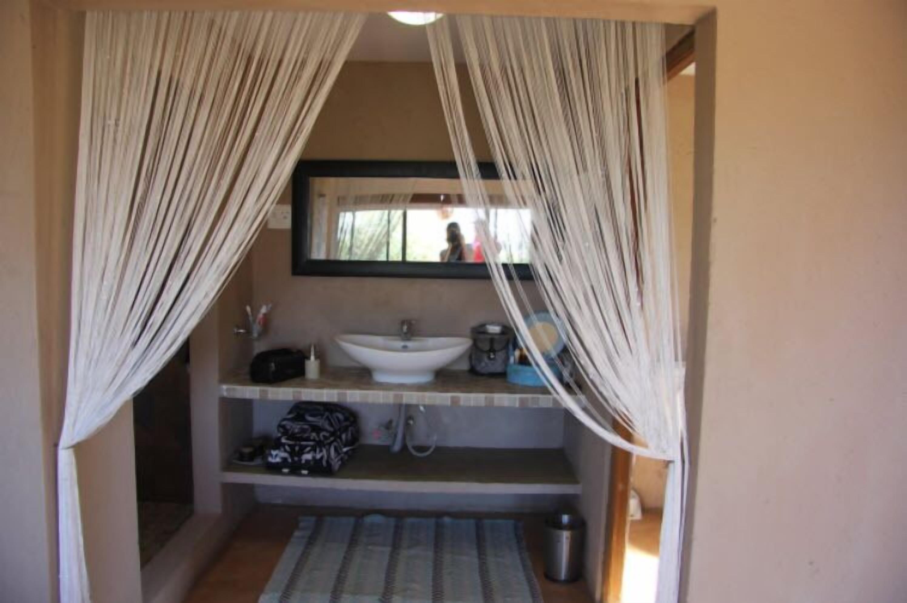 A bathroom with a sink, mirror, and shower area, featuring a window with curtains.
