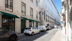 En gade med parkerede biler og bygninger, herunder et skilt til et indkøbscenter.