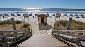 A beach with a wooden staircase leading to a small building, surrounded by blue beach umbrellas and sun loungers. - Master on Gulf -Free round of Golf, Beach Chairs, & Activities Every Day! (Panama City Beach)