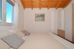 Un dormitorio con techo de madera, una cama con almohadones estampados, un cuadro en la pared y un armario.