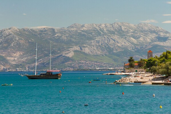 A coastal scene with a boat docked near a rocky shore, a lighthouse, and mountains in the background.