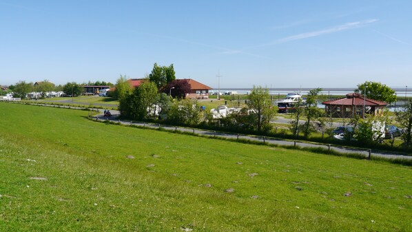 Een grasveld met een gebouw met een rood dak en een klein gebouwtje met een rood dak nabij een waterpartij.