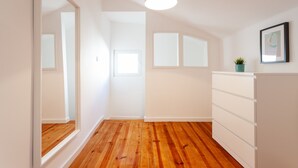 Una habitación con piso de madera, un tocador blanco, una lámpara colgante y un cuadro en la pared.