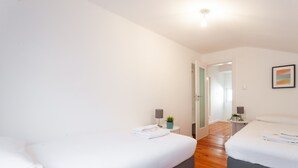 Un dormitorio moderno con dos camas, una mesita de noche con lámpara, una planta en maceta y un cuadro en la pared.