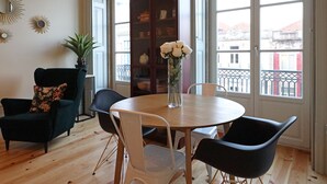 Un comedor con una mesa redonda, sillas blancas, un sillón verde oscuro y una estantería.