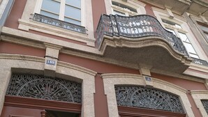 Un edificio con detalles arquitectónicos ornamentales, que incluye un balcón con elaborada rejería y una puerta con cerradura electrónica.