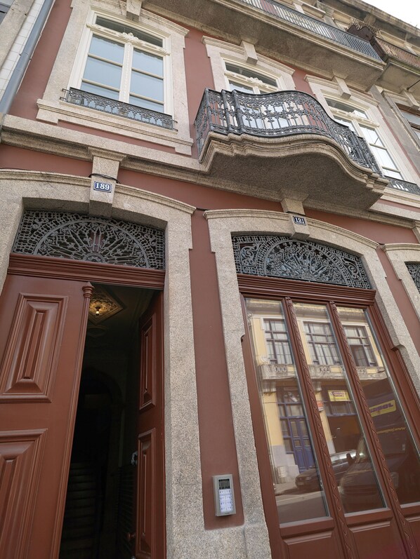 A building with ornate architectural details, including a balcony with intricate metalwork and a door with a keypad lock.