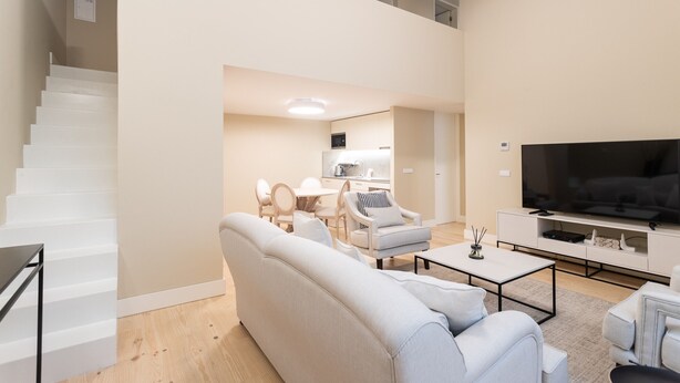 A modern living room with a sofa, coffee table, TV, and a staircase leading to an upper level.