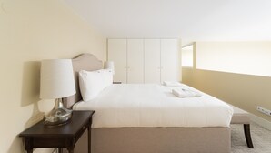 A neatly made bed with white linens and a bedside table with a lamp.