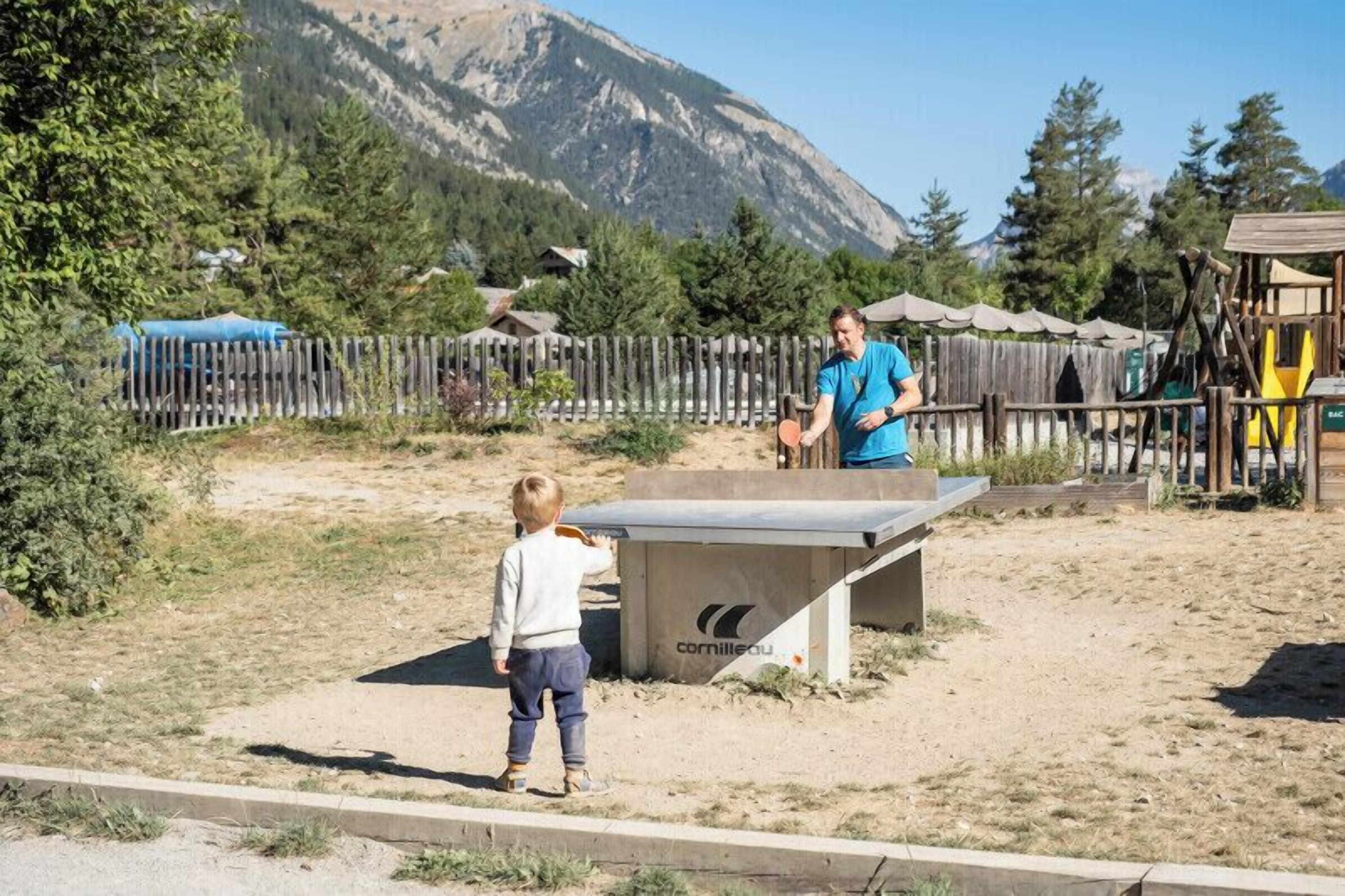 A child playing table tennis in an outdoor area with a mountainous backdrop.