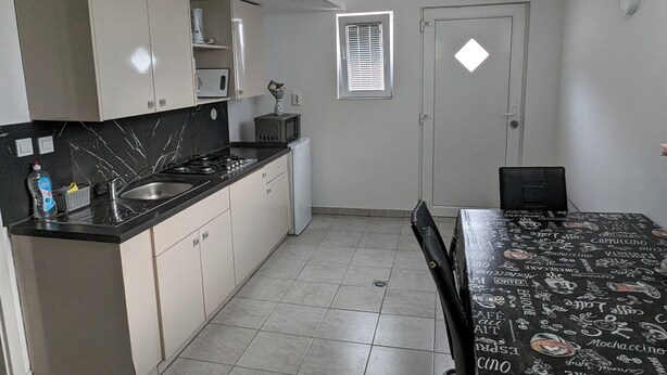 A compact kitchen with a sink, stove, and microwave. There is a dining table with a black tablecloth featuring coffee and tea illustrations. - Apartment Mojca near Bled (Zabreznica)