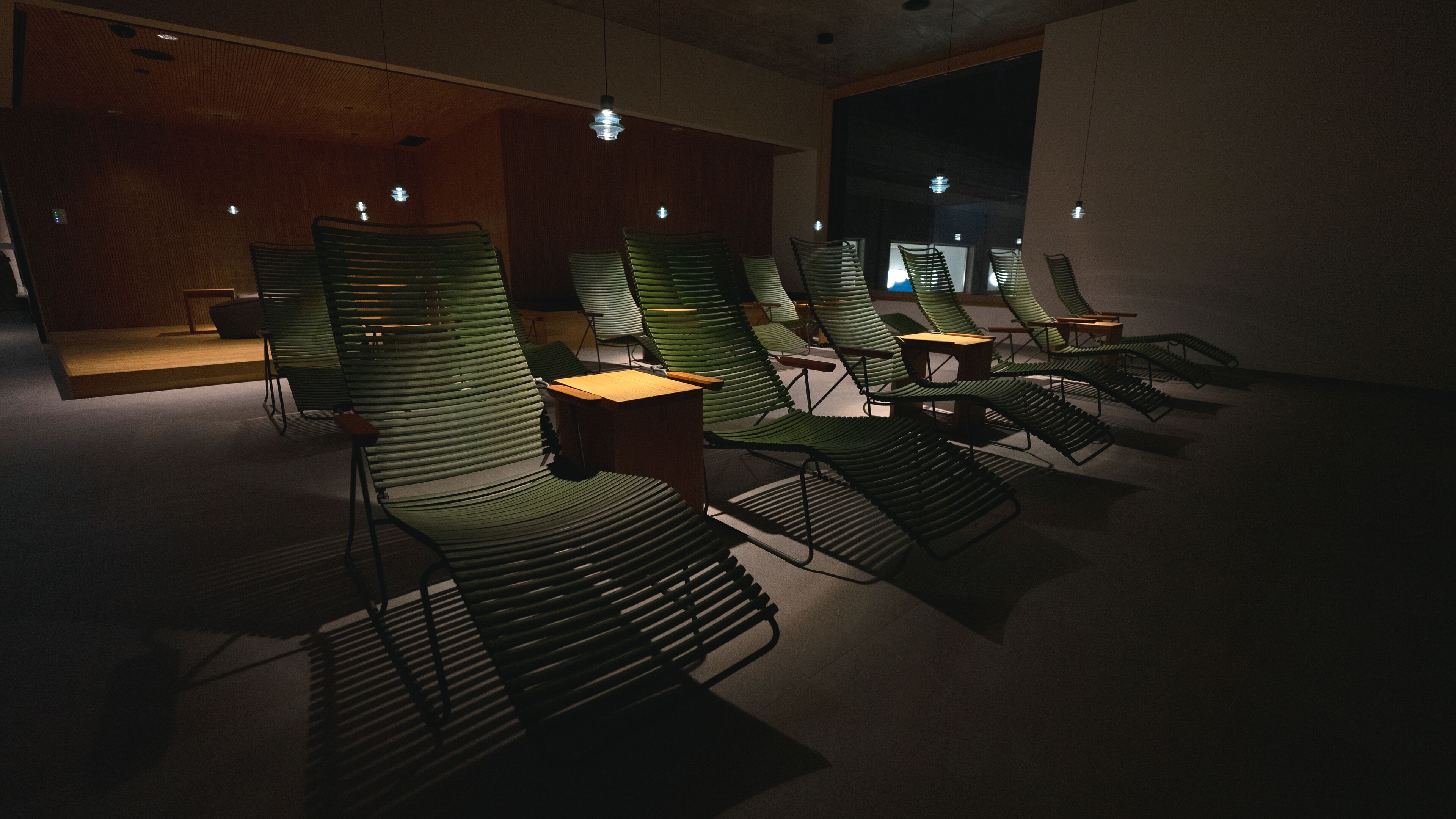 A dimly lit room with several reclining chairs arranged in rows, wooden paneling on the walls, and a large window in the background.