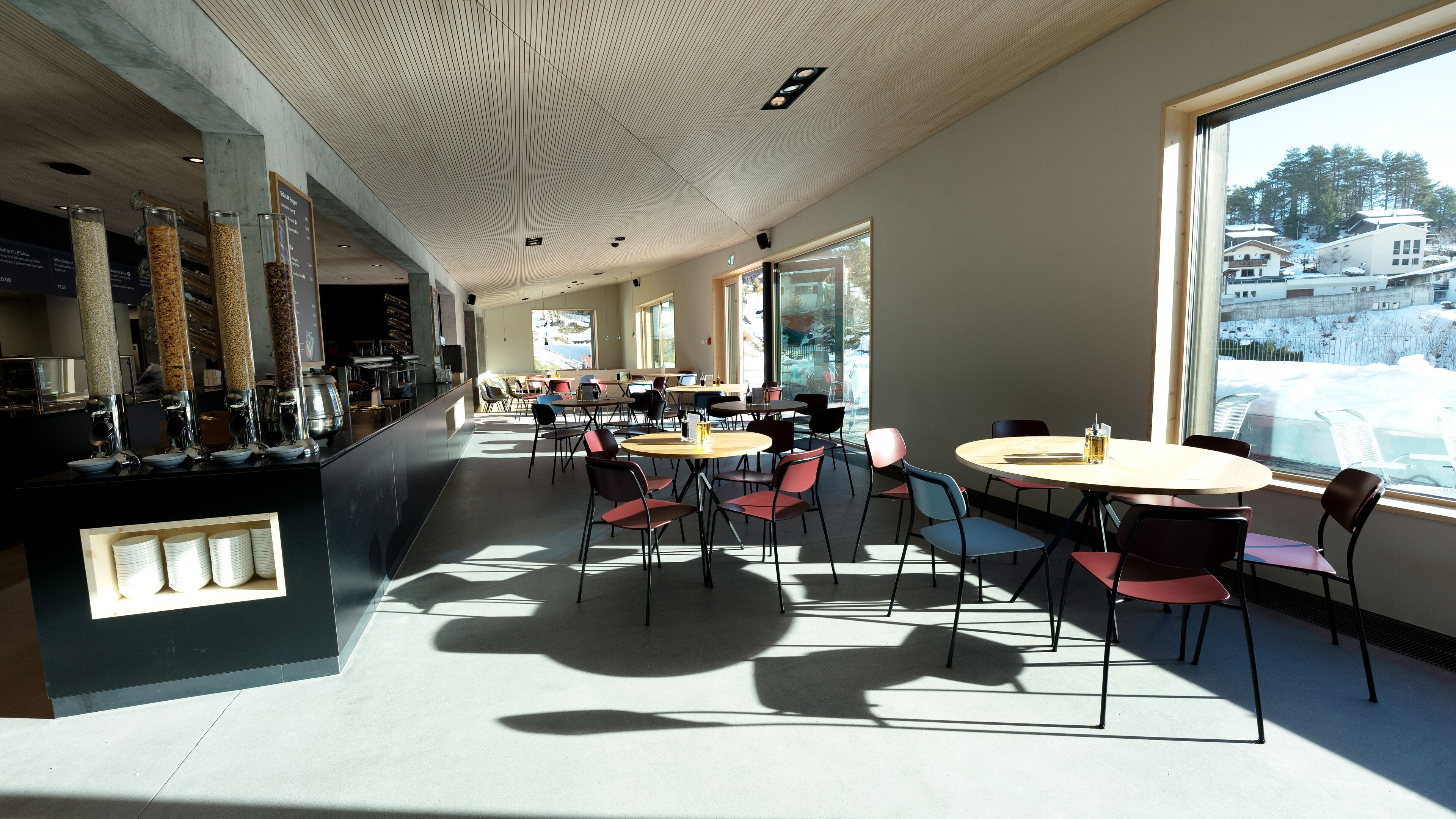 Una cafetería moderna con una barra larga, varias zonas de estar y grandes ventanales que ofrecen vistas a un paisaje nevado.