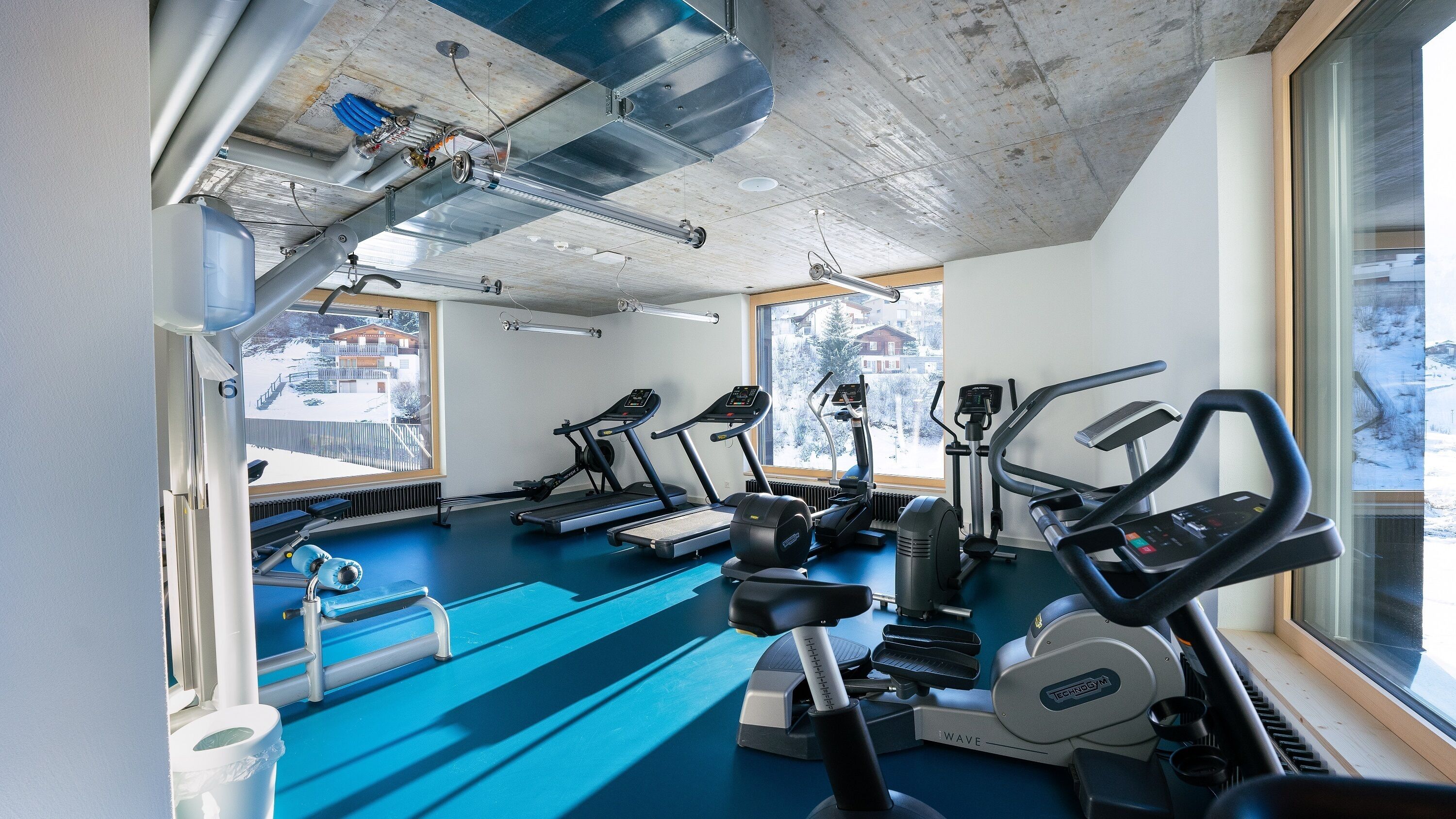A gym with treadmills, elliptical machines, and a blue floor.