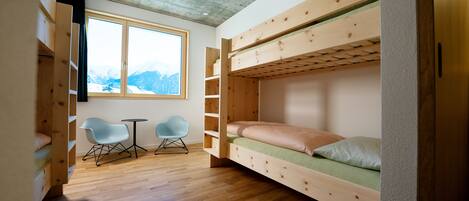 A cozy room with a bunk bed, two chairs, a small table, and a large window with a mountain view.