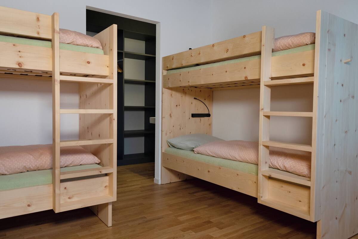 Duas camas beliche com gavetas para armazenamento, soalho de madeira e uma porta que dá para outro quarto.