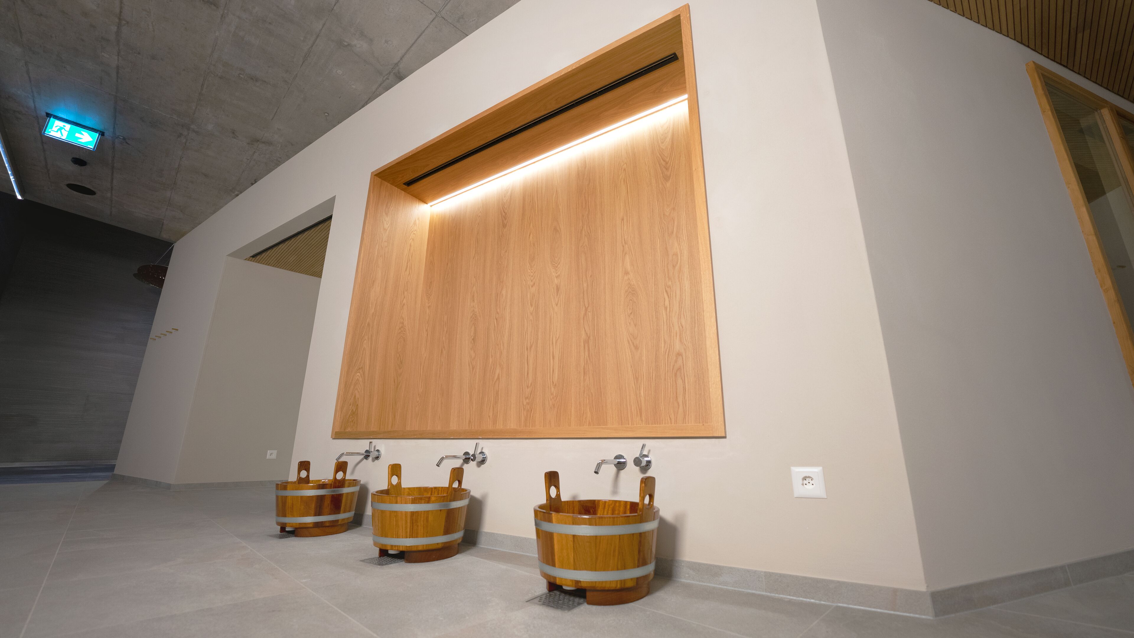 A restroom with three wooden buckets as sinks, a large wooden panel above the sinks, and a ceiling light.