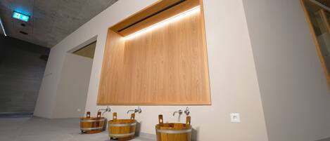 A restroom with three wooden buckets as sinks, a large wooden panel above the sinks, and a ceiling light.