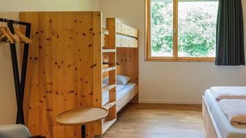 Ein Zimmer mit einem Etagenbett, einem kleinen runden Tisch und einem Fenster mit Blick auf Bäume.