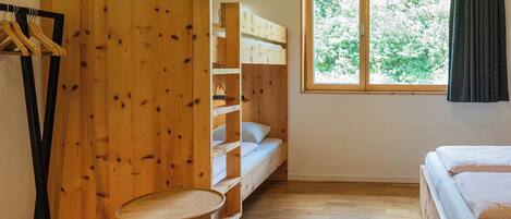Een kamer met een stapelbed, een klein rond tafeltje en een raam met uitzicht op bomen.