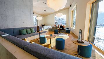 A modern interior with a grey sofa, round tables, and large windows offering a view of a snowy landscape.