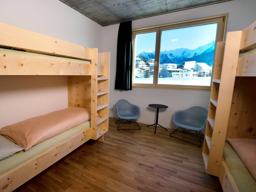 Une chambre avec un lit superposé, une fenêtre donnant sur les montagnes, deux chaises et une petite table.