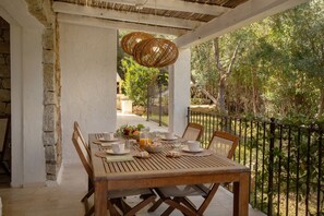 Une table en bois, dressée pour le petit-déjeuner, avec vue sur des arbres et un mur de pierres.