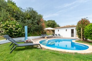 A swimming pool with lounge chairs, a table with drinks, and a white building with a tiled roof. - VILLA GELSOMINO, 500 meters from the sea with garden, private pool, and sea view (Castiadas)