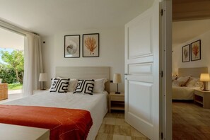 Ein Hotelzimmer mit einem großen Bett, einem Nachttisch, einer Lampe und einer Tür zu einem anderen Raum.